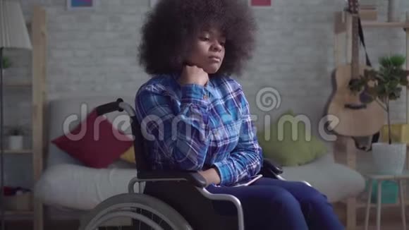 孤独而悲伤的美国黑人妇女一个人坐在轮椅上留着非洲发型视频的预览图