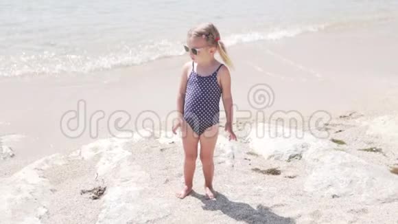 小美丽的女儿穿着太阳镜坐在海滩上的泳衣视频的预览图