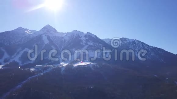 在一个充满活力的冬日滑雪场的空中景色剪辑在蓝蓝的晴空上飞过雪山视频的预览图