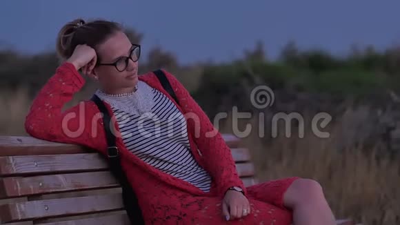 戴眼镜的女孩坐在长凳上看傍晚的大海视频的预览图