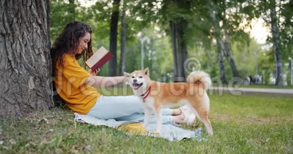 可爱的女孩在公园享受书的侧面景色微笑着抚摸着纯种狗视频的预览图