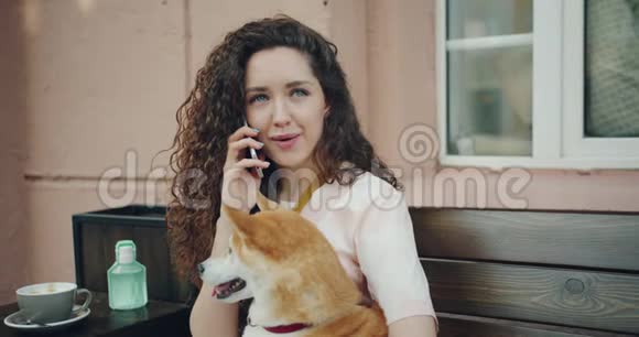 女孩在户外咖啡馆里用手机说话和拥抱宠物狗的慢动作视频的预览图