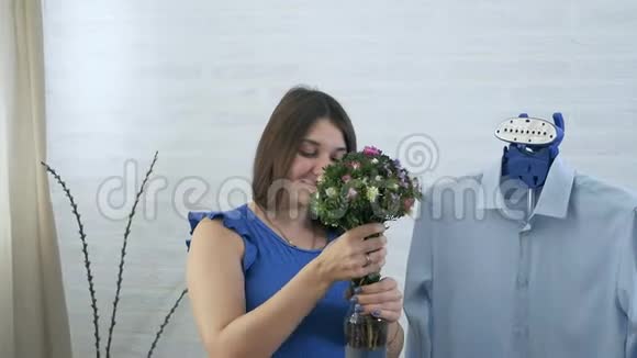手里拿着花的年轻女子蒸衣服蒸的过程蓝色的细节家庭护理和罗曼蒂克a视频的预览图