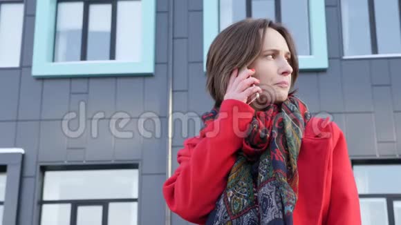 这段视频讲述的是一位年轻的商务女性穿着红色外套和围巾在现代办公大楼里打电话视频的预览图