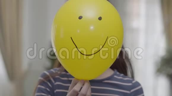 一个漂亮的女孩躲在黄色气球后面上面画着一张快乐的脸然后把它放下孩子在微笑视频的预览图