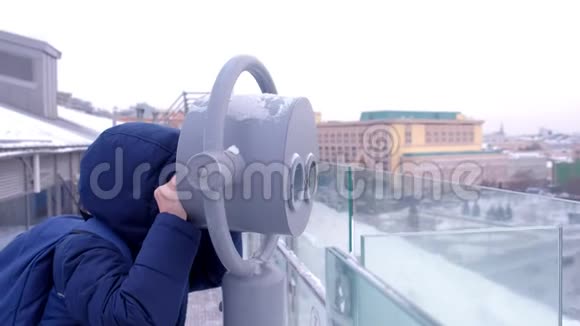 冬天小男孩在城市的楼顶上用双筒望远镜观察视频的预览图