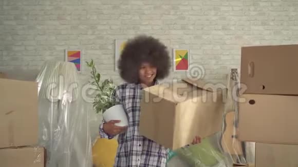 非洲女人留着非洲发型手里拿着一株植物搬到了一间新的现代公寓里视频的预览图