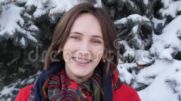 这个视频是关于美丽的年轻白种人女人裹着温暖的红色外套带着围巾带着牙套对着镜头微笑视频的预览图