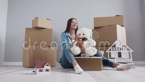 可爱的幸福的年轻女子坐在地板上在搬到她的新公寓后打开纸箱视频的预览图