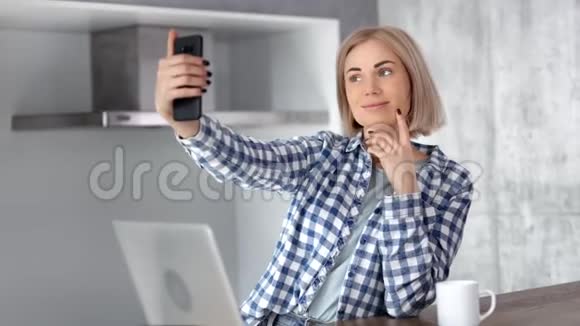 年轻漂亮的休闲笑脸女人在现代家庭厨房用智能手机自拍视频的预览图