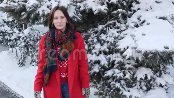 美丽的年轻黑发女人穿着红色外套围巾手套微笑着冻僵了试图热身双手吹在外面的冬天视频的预览图
