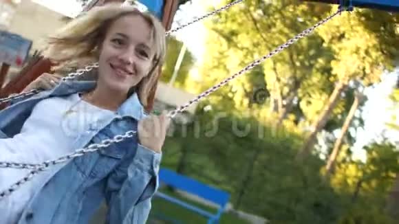 快乐美丽的女孩在秋千上在他房子的背景下金发女孩笑着对着一个孩子笑笑视频的预览图