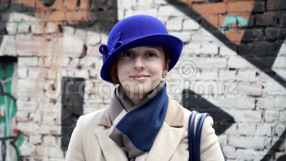 女士戴着蓝帽子背景墙涂鸦特写可爱微笑看镜头4K视频的预览图