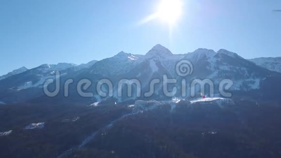 在一个充满活力的冬日滑雪场的空中景色剪辑在蓝蓝的晴空上飞过雪山视频的预览图