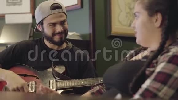 年轻的笑着留着胡须的男人在酒吧里弹吉他迷人的丰满女人坐在旁边唱歌酒吧休闲视频的预览图