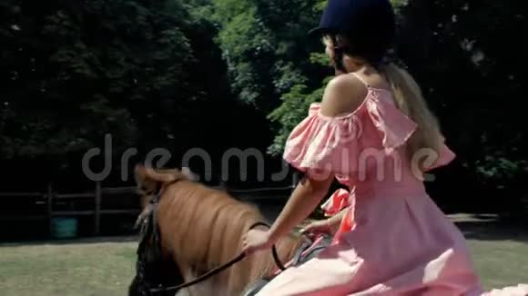 一个十几岁的女孩戴着保护头盔和粉红色的连衣裙骑着一匹棕色的马在树的背景上侧视4k4k视频视频的预览图