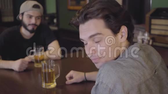 两个男人坐在酒吧里一起喝啤酒大家一起喝啤酒玩得很开心一个人看着视频的预览图