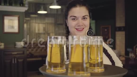 肖像丰满的女人扎着辫子穿着白色衬衫拿着托盘三个啤酒杯对着镜头微笑休闲视频的预览图