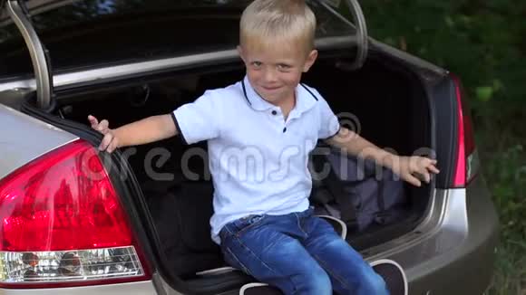 汽车后备箱里一个可爱的小男孩的肖像家庭旅行道路视频的预览图