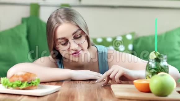 微笑滑稽的年轻女人在餐桌上玩手指选择健康和不健康的食物视频的预览图