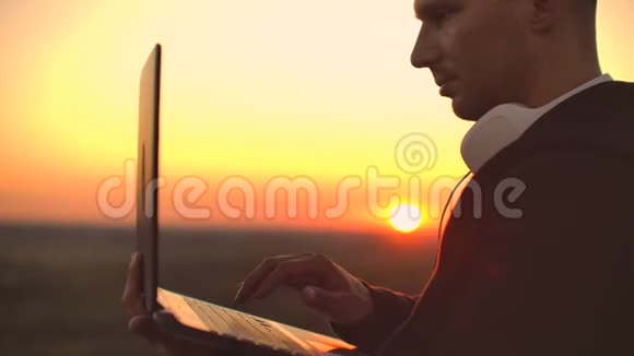 一个男人戴着白色的大耳机手指放在笔记本电脑的键盘上站在大楼的屋顶上视频的预览图