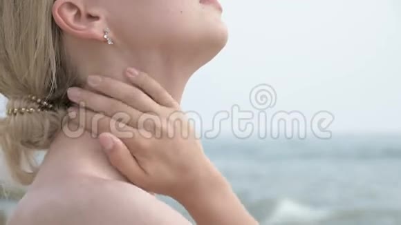 特写镜头一个年轻迷人的女孩戴着墨镜脖子上涂着防晒霜坐在海边视频的预览图