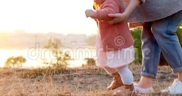 一位年轻的母亲和她的女儿在新鲜的空气中散步日落时分幸福的家庭在绿草上散步视频的预览图