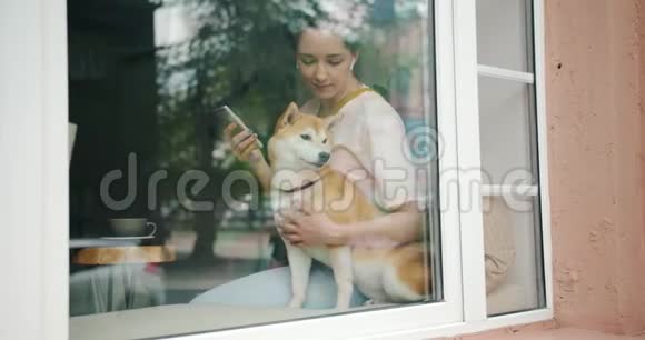 女士在咖啡馆里用耳机和智能手机亲吻狗听音乐视频的预览图