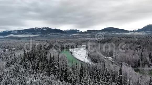 在一个寒冷的冬日无人机照相机穿过一片茂密的森林带着一个翠绿的池塘和一条靠近山脉的公路视频的预览图
