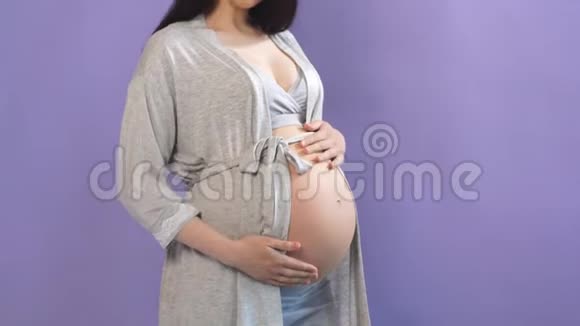 幸福的未来妈妈摆姿势用手在裸露的腹部在紫色的背景上视频的预览图