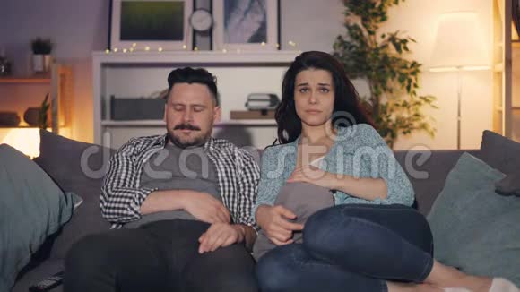 丈夫和妻子坐在家里的沙发上看电视上的戏剧视频的预览图