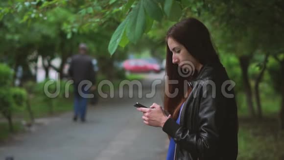 春天迷人的女孩坐在户外在手机上浏览网视频的预览图