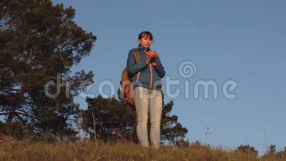 远足女孩喝热茶看日落女旅行者站在山顶上用玻璃喝咖啡视频的预览图