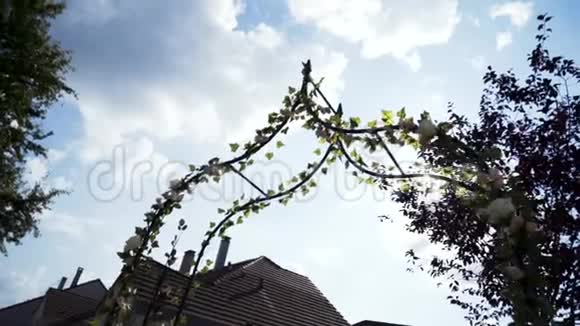 在背景婚礼和婚礼上用蓝色多云的天空装饰玫瑰花的婚礼拱门的底部景色视频的预览图