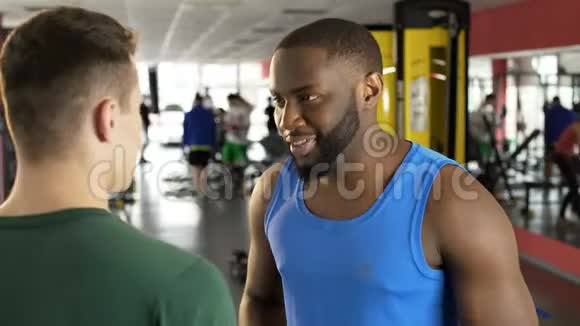 微笑的非裔美国人在健身房和健身教练交谈运动视频的预览图