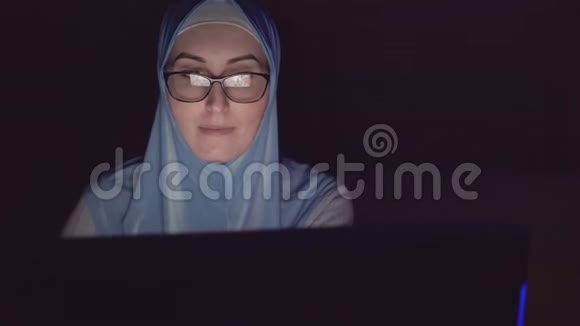 穆斯林妇女戴头巾戴眼镜夜间使用电脑的肖像视频的预览图