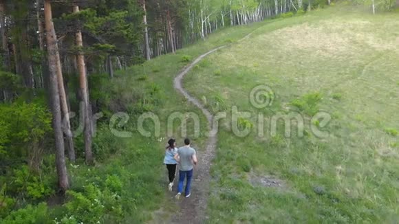 一对年轻夫妇在森林小径上奔跑的航拍镜头视频的预览图