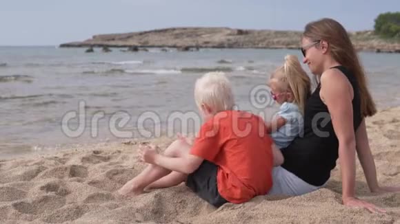 美丽的母亲和孩子们坐在海滩上看着大海视频的预览图