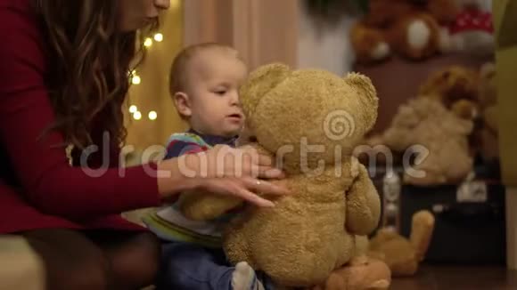 近距离观看小可爱的孩子在家玩大泰迪熊母亲坐在儿子身边手里拿着摇晃的玩具视频的预览图