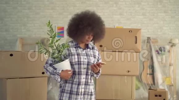 非洲女人发型是非洲式的手里拿着一株植物手里拿着电话挨着箱子移动视频的预览图