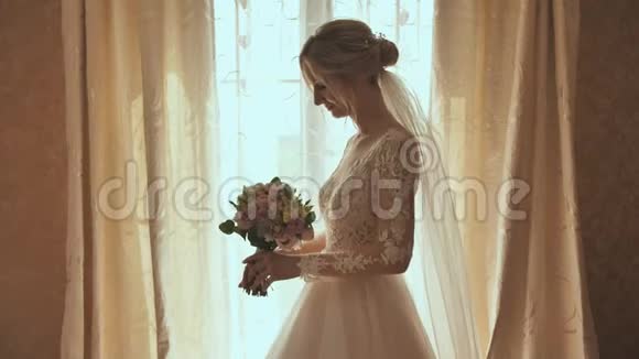 美丽的金发新娘在窗边捧着花束视频的预览图