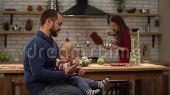 大胡子的父亲和小儿子玩坐在桌子旁妻子做饭午餐快乐视频的预览图