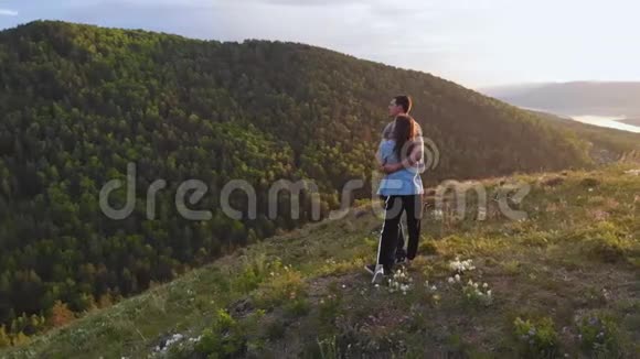 日落时分一对年轻情侣在山顶上的航拍镜头视频的预览图