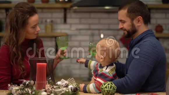 母亲父亲和婴儿坐在现代厨房的桌子上的肖像爸爸抱着可爱严肃的孩子小儿子视频的预览图