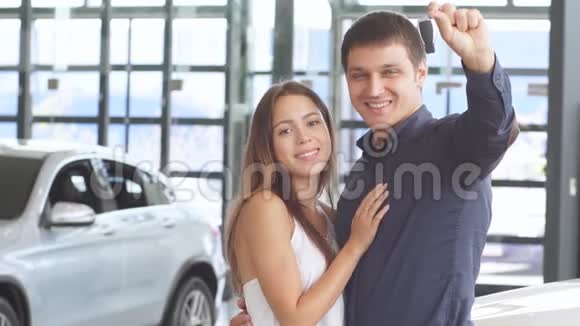 一个英俊的白种人男子手里拿着汽车钥匙和他漂亮的女朋友在新的豪华轿车旁摆姿势视频的预览图