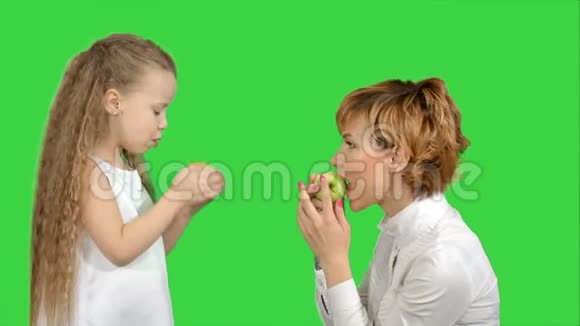 一位年轻的母亲和她的小女儿在绿色屏幕上吃苹果的肖像ChromaKey视频的预览图