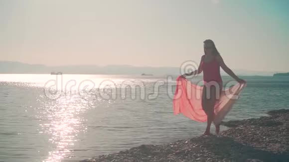 一个穿着红色一件泳衣的怀孕女孩在夕阳的照耀下沿着海滨散步视频的预览图