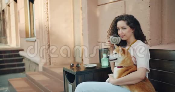 女青年在户外喝茶抱抱石坝犬的慢动作视频的预览图
