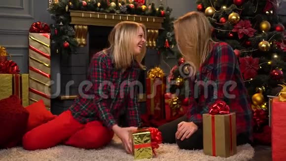 两个穿着红衬衫戴着滑稽帽子的滑稽少女坐在新年或圣诞树旁与圣诞节开怀大笑视频的预览图