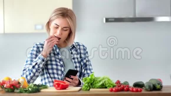 中型特写迷人的年轻素食主义者吃新鲜蔬菜用智能手机聊天视频的预览图